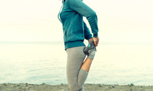 Young woman stretching her legs and preparing to run on coast in summer in the morning, face is not visible. Concept of sport and healthy lifestyle